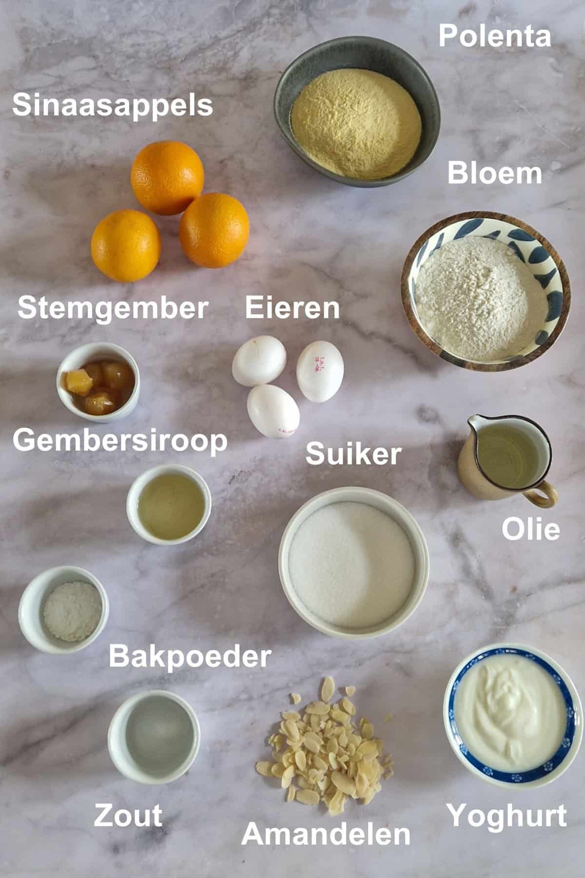 De ingrediënten om polenta cake met sinaasappel en gember te maken, uitgestald op een lichte ondergrond.
