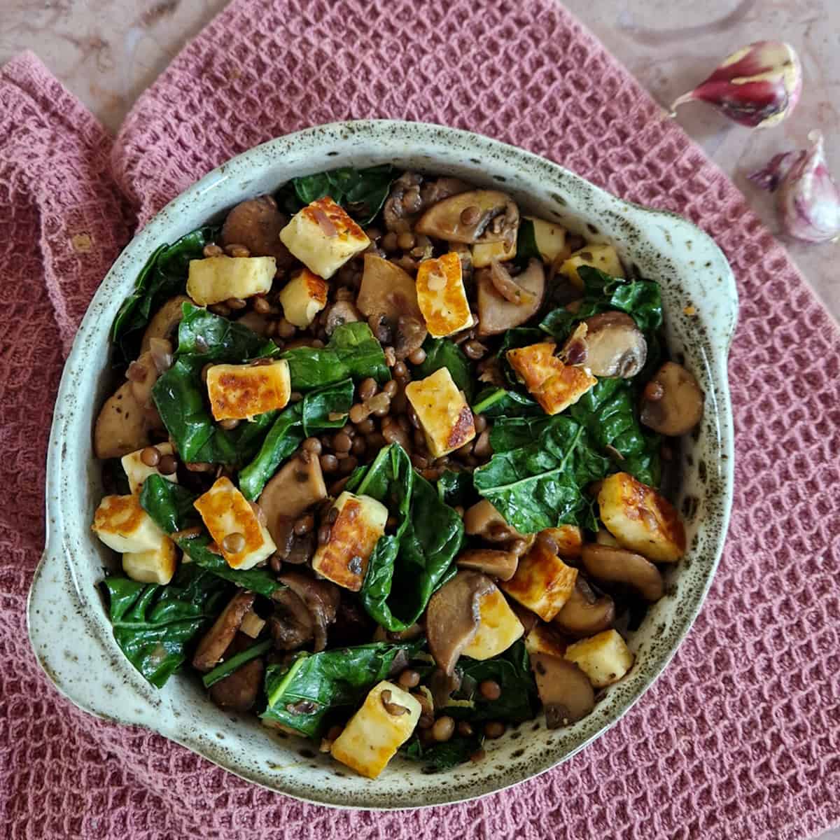 Een kom met palmkoolsalade met halloumi, linzen en kastanjechampignons.