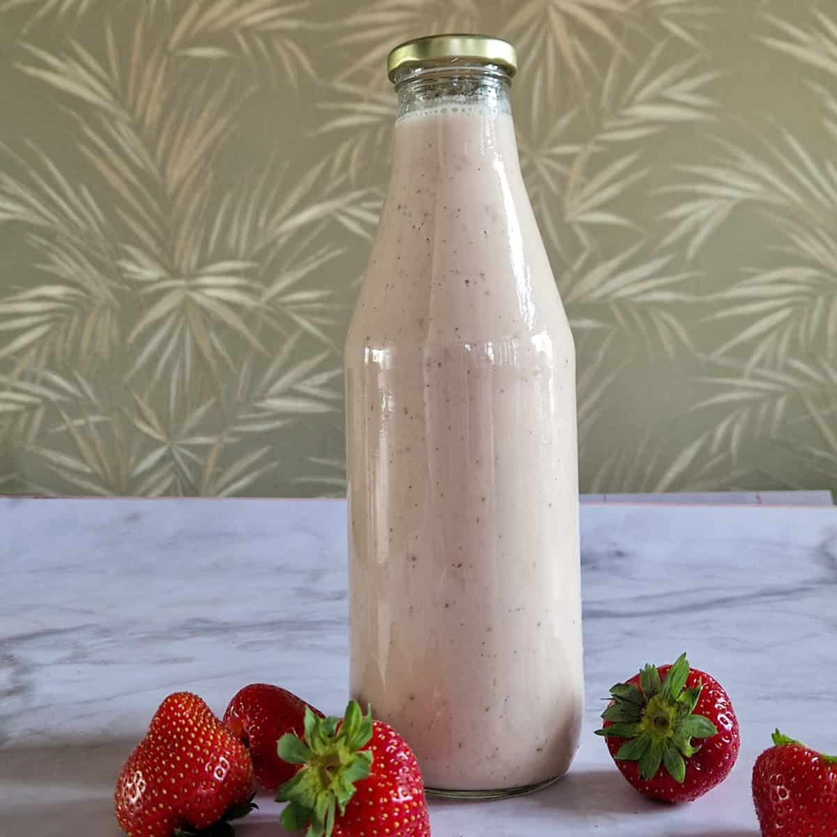 Een fles zelfgemaakte aardbeienvla, met verse aardbeien ernaast ter decoratie.