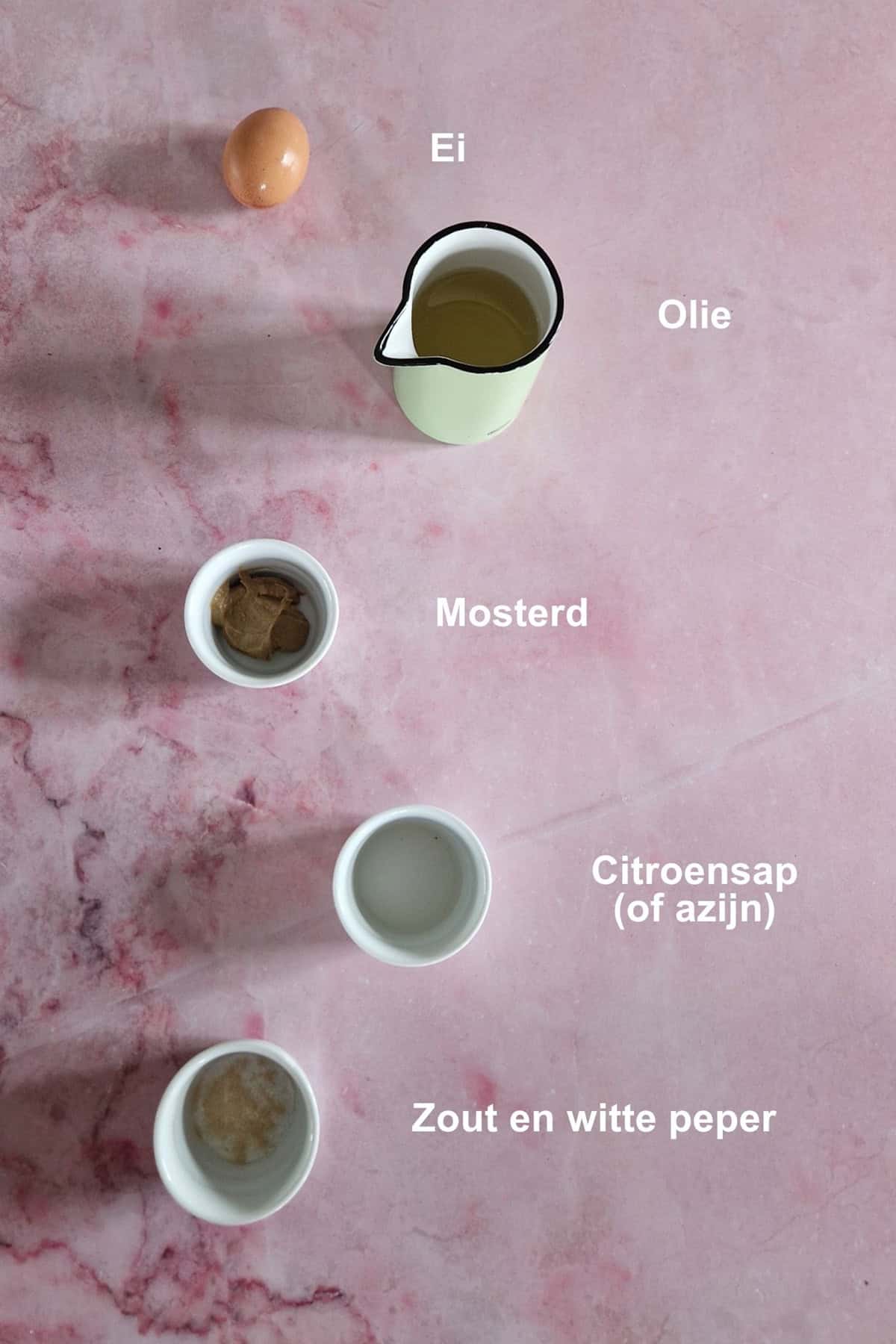 De ingrediënten om zelf mayonaise te maken, uitgestald op een lichtroze, marmeren ondergrond.