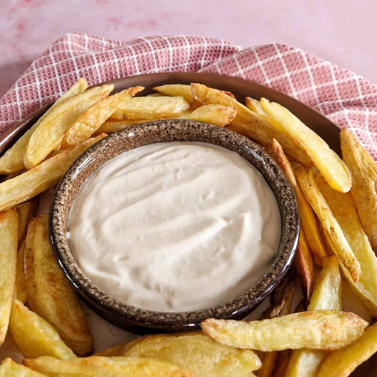 Een bakje zelfgemaakte mayonaise, met gebakken aardappels uit de oven er omheen.