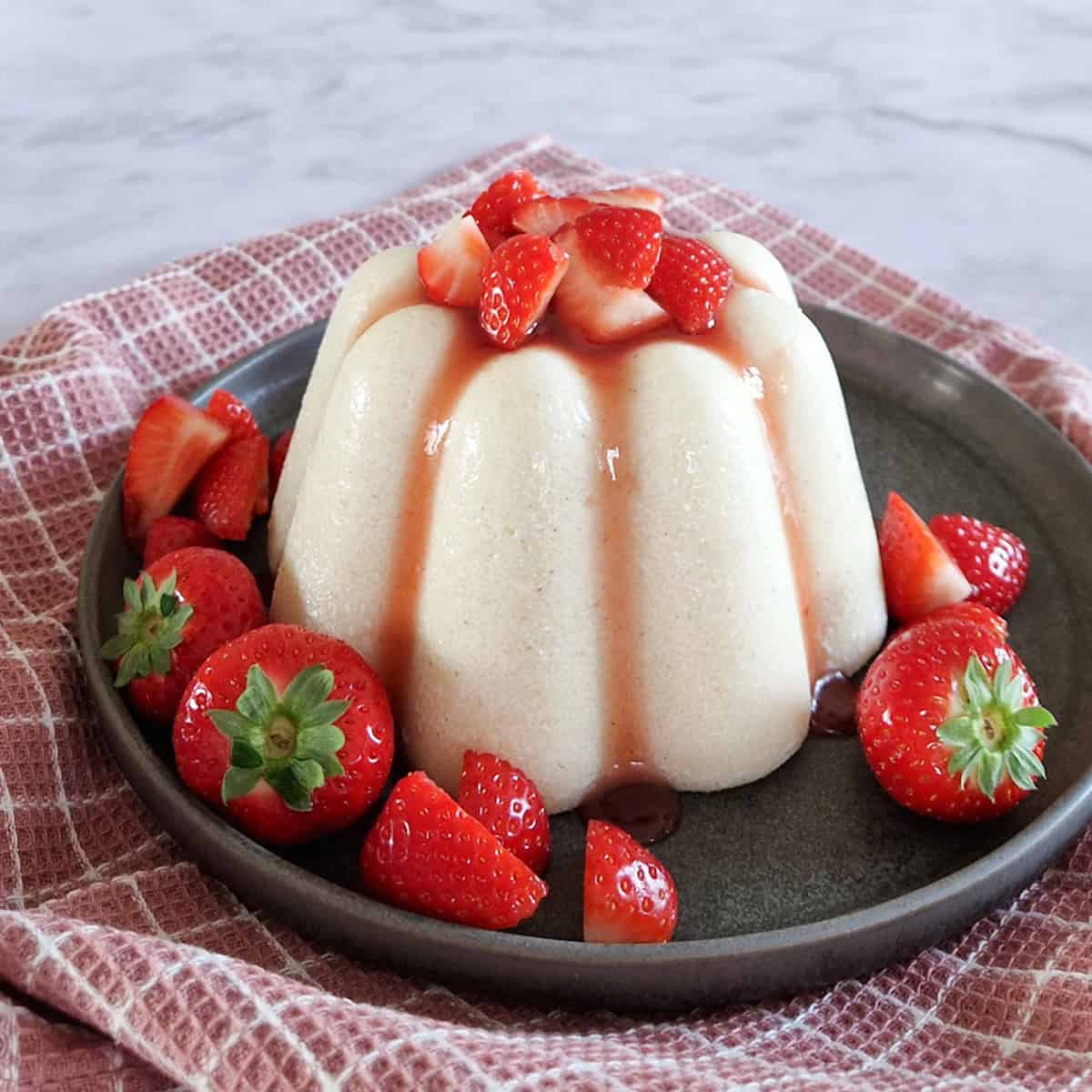 Een ouderwetse griesmeelpudding op een grijs bord. De pudding is gegarneerd met aardbeiensaus en verse aardbeien.