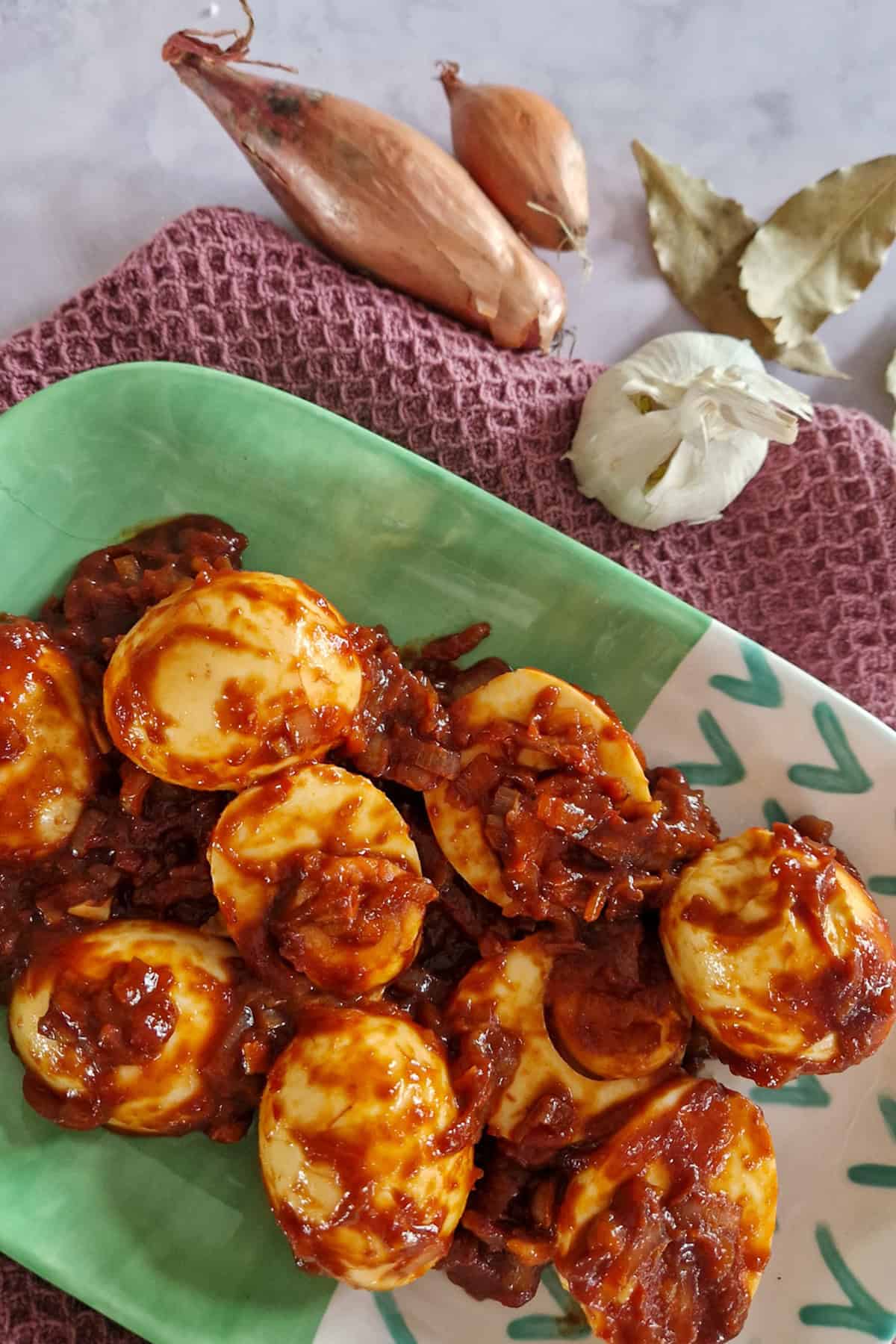 Een bord gevuld met pittige Indische eieren, met op de achtergrond sjalotten en knoflook.