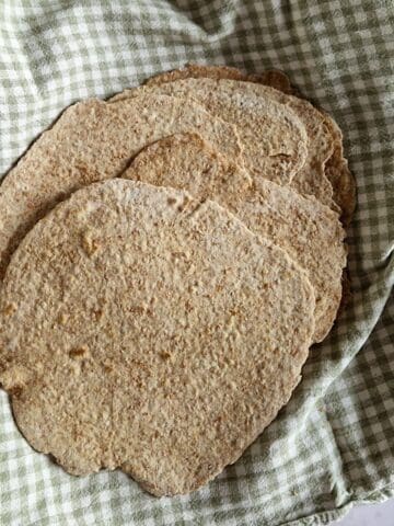 Een mand gevuld met zelfgemaakte volkoren wraps. De wraps liggen op een geblokte groene theedoek.