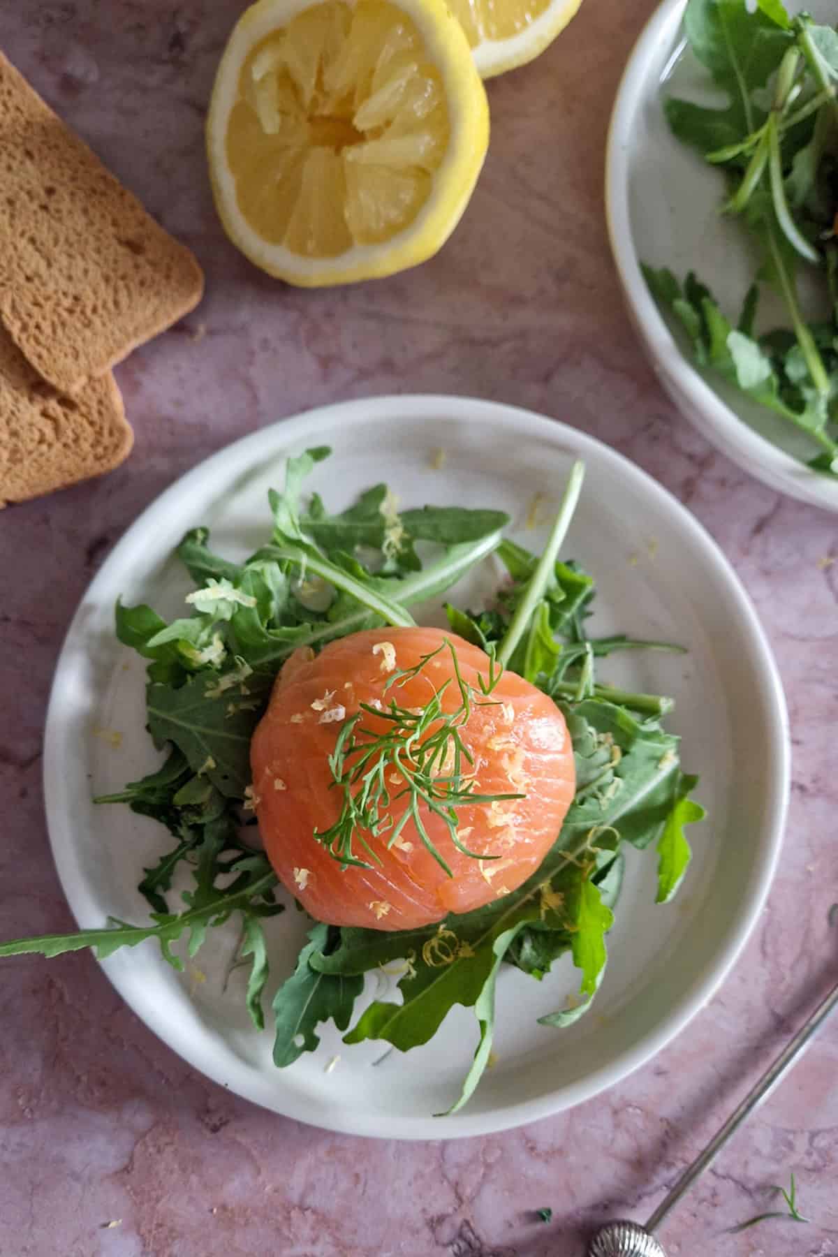 Close up van een gerookte zalmbonbon op een bordje. Het gerecht ligt op een bedje van rucola.
