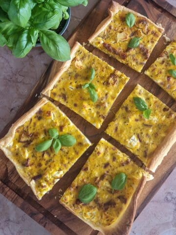 Plaattaart met pompoen en feta, de taart is in zes stukken gesneden en bestrooid met verse basilicum.