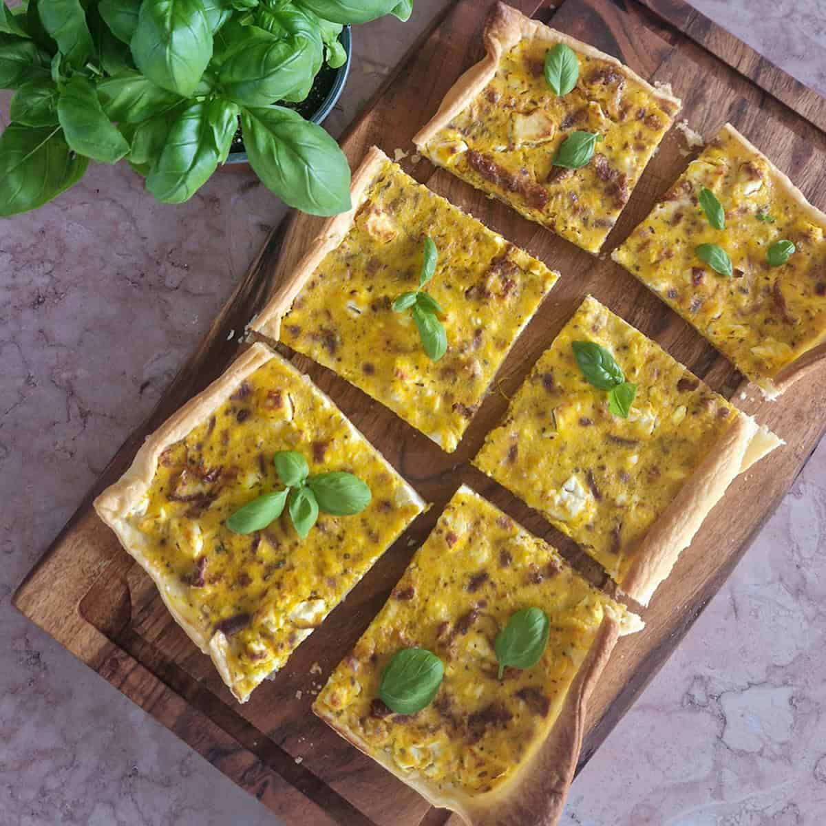 Plaattaart met pompoen en feta, de taart is in zes stukken gesneden en bestrooid met verse basilicum.