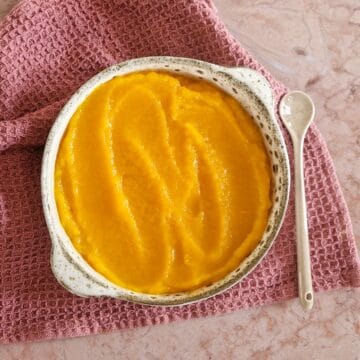 Een kom met zelfgemaakte pompoenpuree, op een paarse stoffen doek.