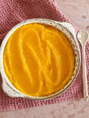 Een kom met zelfgemaakte pompoenpuree, op een paarse stoffen doek.