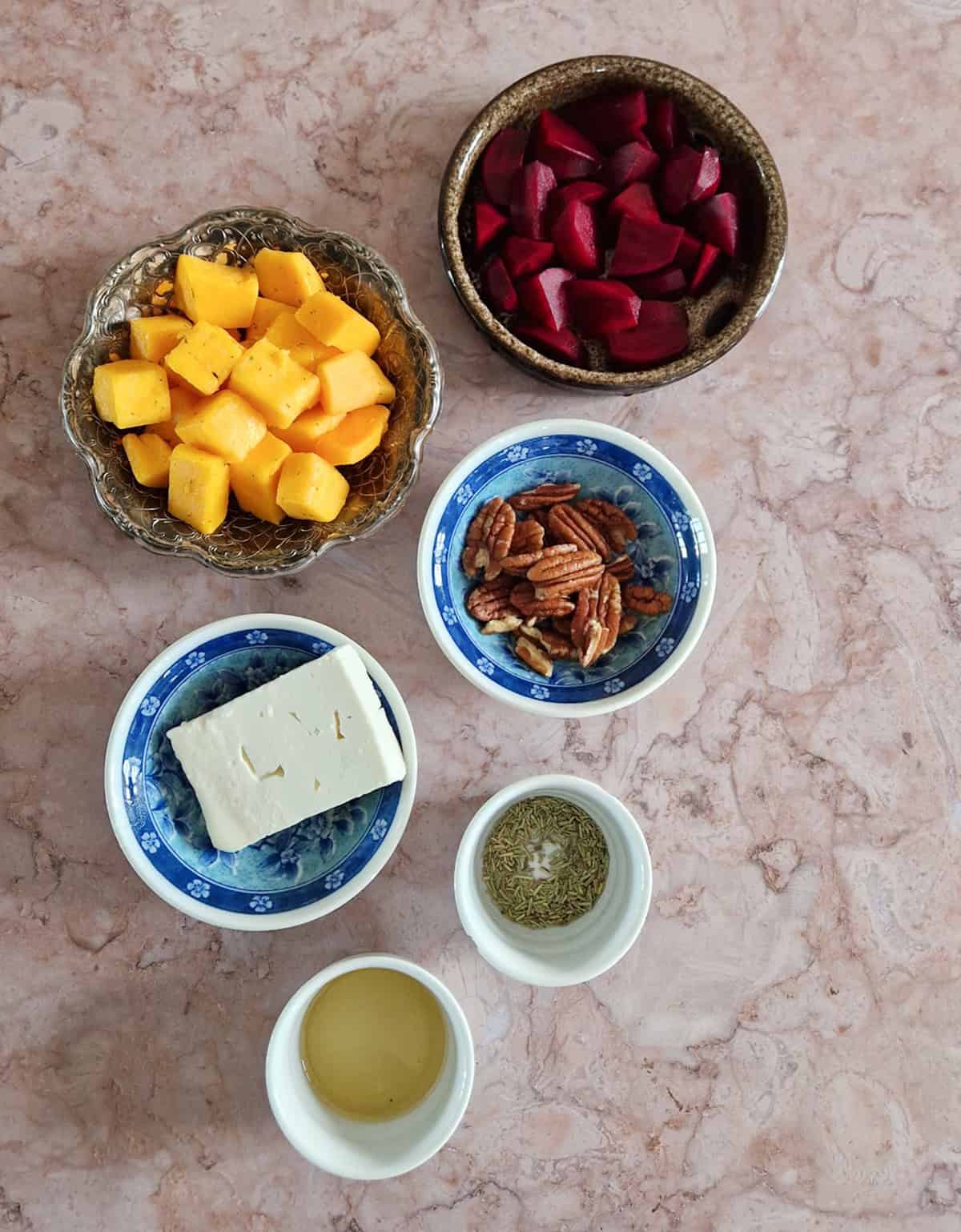 De ingrediënten voor een ovenschotel met pompoen en feta, uitgestald op een bruin-marmeren ondergrond.