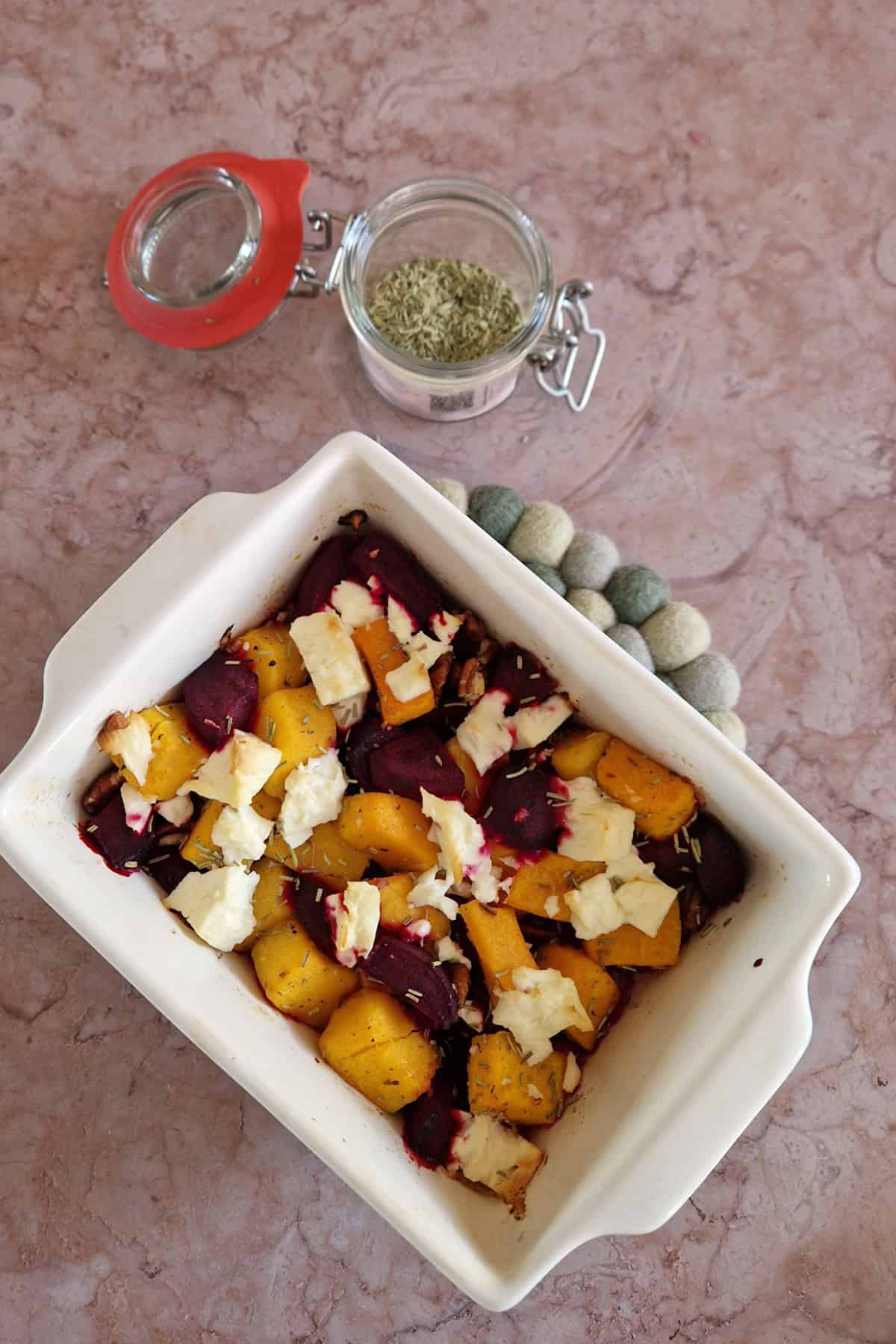 Uitgezoomde foto van een pompoenschotel uit de oven, met bietjes, feta en pecannoten.