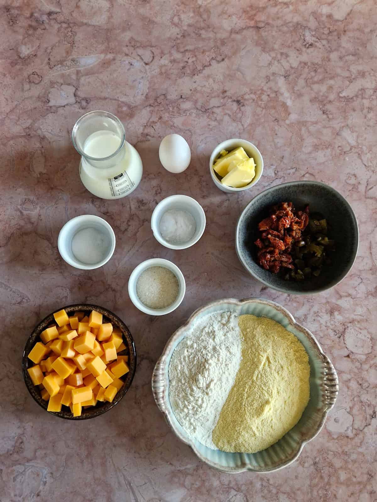 De ingrediënten om jalapeno-maisbrood te maken, uitgestald op een bruin-marmeren ondergrond.
