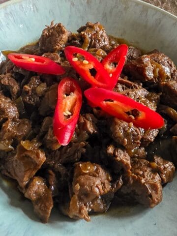 Een portie daging smoor in een licht gekleurde kom. Het stoofvlees gerecht is gegarneerd met rode pepers.