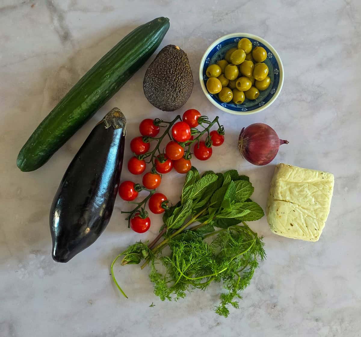 De ingrediënten voor aubergine salade, uitgestald op een wit marmeren ondergrond.