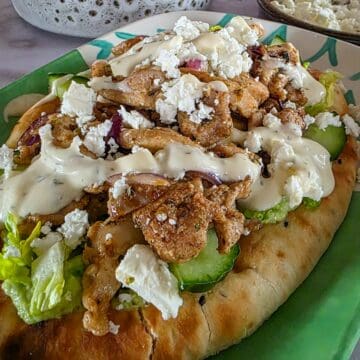 Griekse kip met gyroskruiden op een flatbread, geserveerd met een simpele groene salade, feta en knoflooksaus.