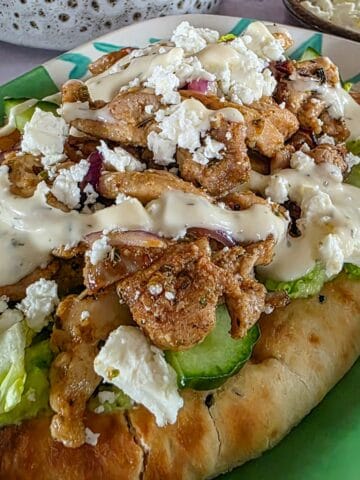 Griekse kip met gyroskruiden op een flatbread, geserveerd met een simpele groene salade, feta en knoflooksaus.