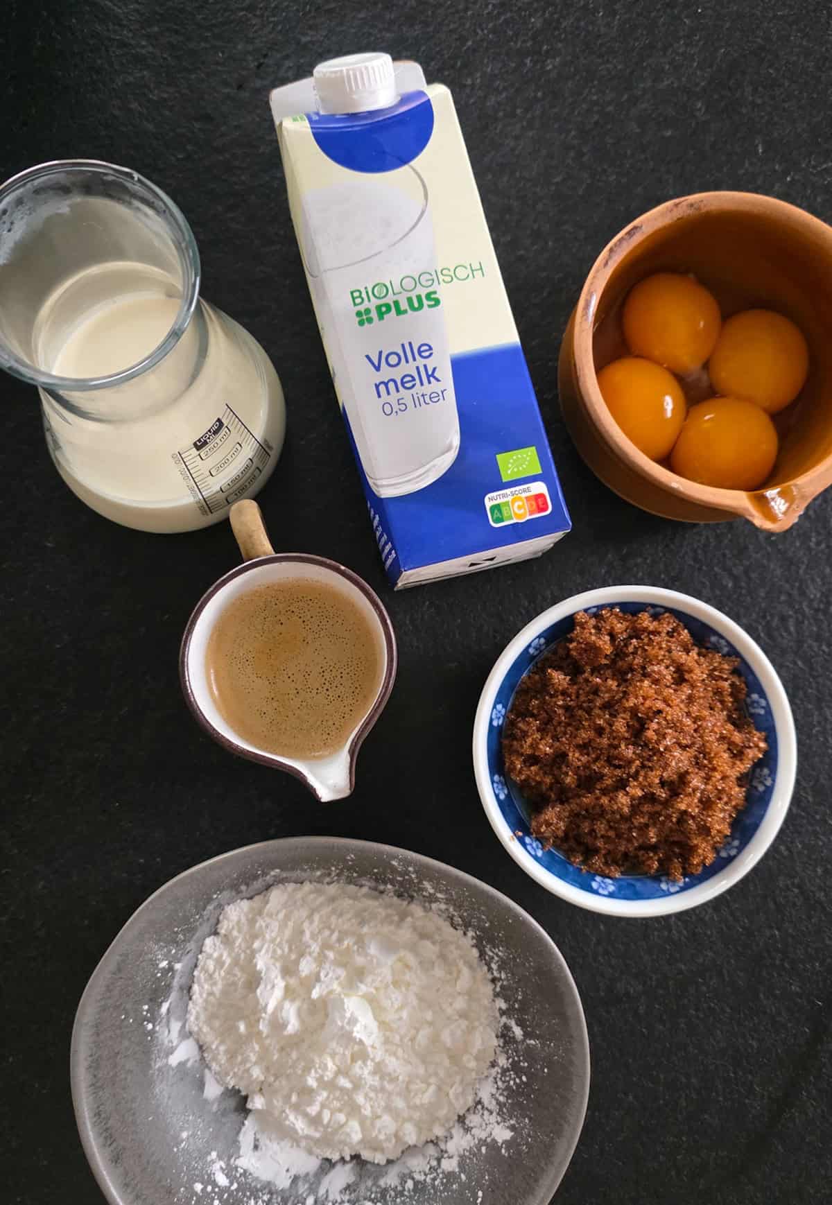 De ingrediënten om hopjesvla te maken, uitgestald op een zwart-natuurstenen ondergrond.