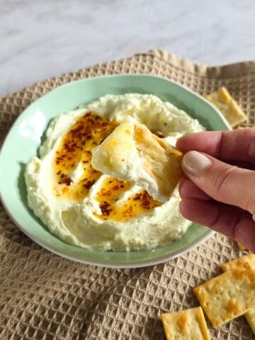 Een hand dipt een toastje in een smeersels voor op stokbrood (whipped feta met hot honey).