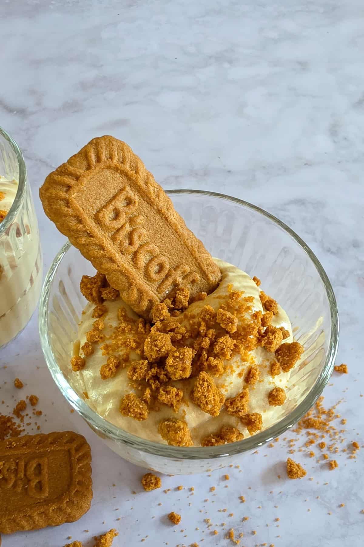 Een glas met een speculoos dessert, je ziet de bovenkant van het toetje, met speculoos kruimels en een Lotus Biscoff koekje.